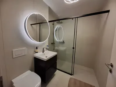 Badezimmer mit Glasdusche und rundem Leuchtspiegel